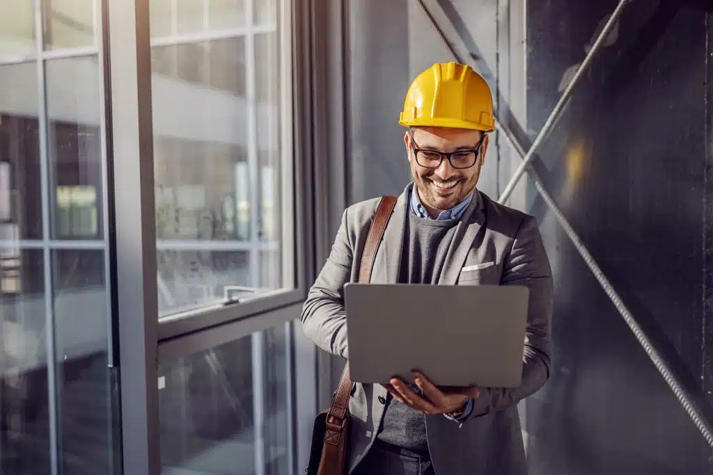 Een medewerker met een veiligheidshelm op en een laptop in de hand