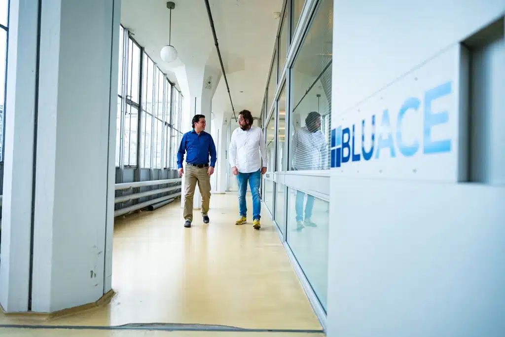 Een foto van twee medewerkers die op de gang van het Bluace kantoor lopen